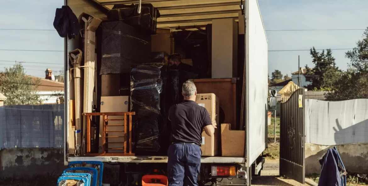 melhores empresas de mudanças: caminão de mudança com a traseira aberta e um homem colocando ou retirando objetos de dentro.