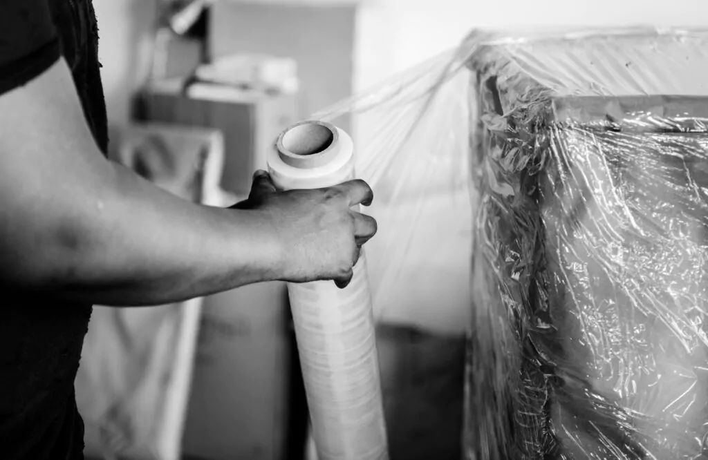 Homem embalando móveis com papel plástico.